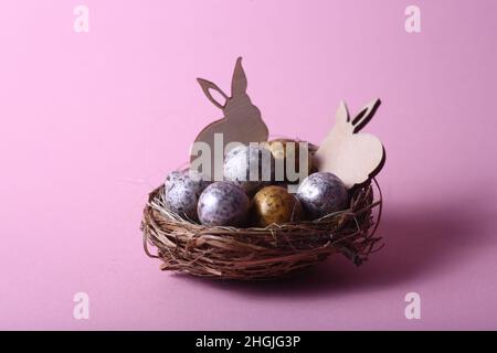 Osterkonzept - zwei Kaninchen in einem Nest mit Schokoladeneiern vor rosa Hintergrund. Horizontales Bild. Das Bild enthält den Kopierbereich Stockfoto