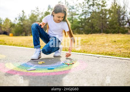 Teenager-Mädchen, das am Sommertag eine regenbogenfarbene Kreide auf den Asphalt zeichnet Stockfoto