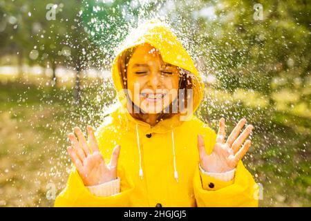 Lächelndes Mädchen im Teenageralter, das an regnerischen Tagen im Freien Regenmantel trägt Stockfoto