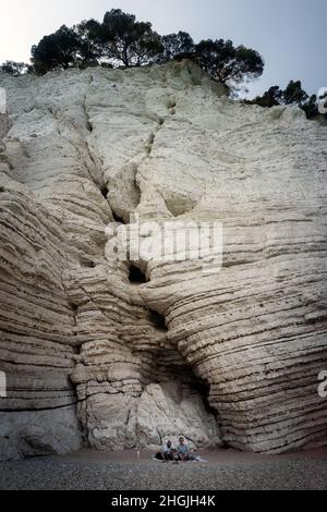 Strand von Vignanotica, Gargano, Apulien, Italien: Ein Mann und eine Frau sitzen auf dem Strand mit der hohen weißen Klippe von Vignanotica hinter sich Stockfoto