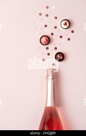 Kreative trendige flache Lay mit rosa und Gold runden Konfetti und Schokolade Süßigkeiten aus Champagner-Flasche auf pastellfarbenem Hintergrund gegossen. Flach liegend, Draufsicht, Kopierbereich. Grußkarte zum Valentinstag. Stockfoto