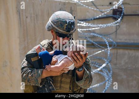 210821-M-JM820-1025 HAMID KARZAI INTERNATIONAL AIRPORT, Afghanistan (21. August 2021) – Eine US-Marine, die der 24. Marine Expeditionary Unit (MEU) zugewiesen ist, tröstet ein Kleinkind, während es während einer Evakuierung auf dem Hamid Karzai International Airport, Kabul, Afghanistan, am 21. August auf die Mutter wartet. US-Dienstmitglieder unterstützen das Außenministerium bei einer nicht-kämpferischen Evakuierungsoperation (NEO) in Afghanistan. Stockfoto