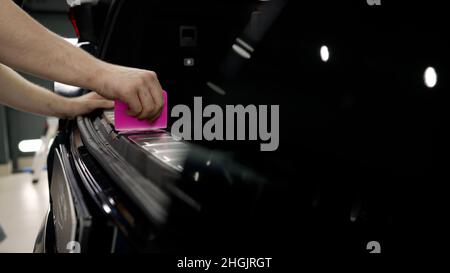 Der Meister klebt den Film in den Kofferraum. Detaillierte Angaben zum Fahrzeug. Der Techniker installiert Vinyl, um den Kofferraumbereich des Kofferraums zu schützen. Stockfoto