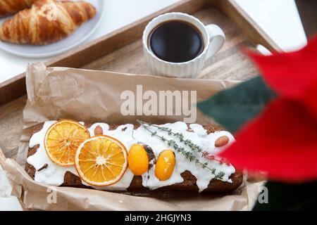 Frisch gebackener weihnachtskuchen und Croissant auf einem grauen runden Teller, eine weiße Tasse Kaffee und eine Girlande auf einem Tablett auf dem Tisch. Blühende Weihnachtssterne. Stockfoto