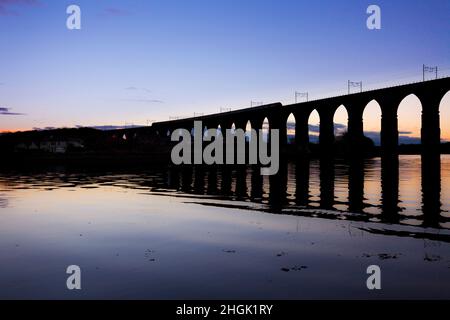 Eine länderübergreifende Züge Intercity 125 Kreuzung die Royal Border Bridge, Berwick upon Tweed mit der Silhouette im Wasser bei Sonnenuntergang widerspiegelt. Stockfoto