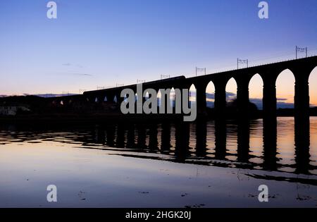 Eine länderübergreifende Züge Intercity 125 Kreuzung die Royal Border Bridge, Berwick upon Tweed mit der Silhouette im Wasser bei Sonnenuntergang widerspiegelt. Stockfoto