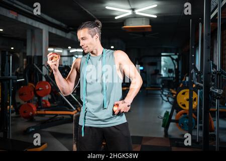 Junge gutaussehende Sportler hungrig und essen gesunde Apfelfrüchte im Fitnessstudio Stockfoto