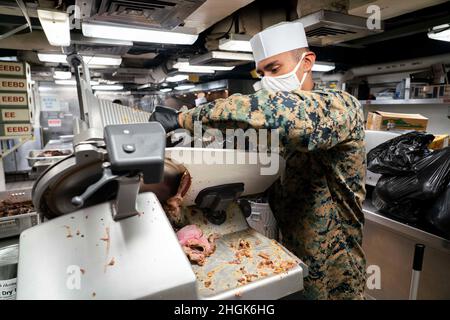 PAZIFIK (28. August 2021) U.S. Marine Corps PFC. Jesus Ojeda, ein Spezialist für Lebensmitteldienstleistungen, der für 1/1 Hauptquartiere und Dienste, 11th Marine Expeditionary Unit (MEU), aus Inglewood, Kalifornien, beauftragt wurde, schneidet Roastbeef an Bord des Amphibiendocks USS Pearl Harbor (LSD 52), August 28. Pearl Harbor, Teil der USS Essex Amphibious Ready Group (ARG), arbeitet zusammen mit der 11th MEU im Verantwortungsbereich der US-Flotte von 7th, um die Interoperabilität mit Verbündeten und Partnern zu verbessern und als ready Response Force zur Verteidigung von Frieden und Stabilität in der Indo-Pazifik-Region zu dienen. Stockfoto