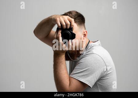 Ein hübscher und selbstbewusster Fotograf mit einer großen professionellen dslr-Kamera, die auf weißem Hintergrund fotografiert. Stockfoto