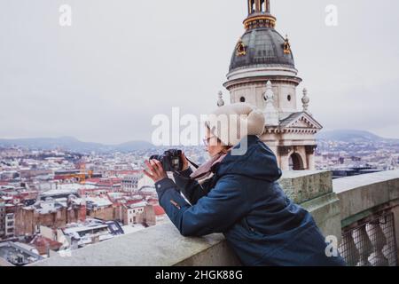 Die Frau fotografiert an einem verschneiten Tag von der St.-Stephens-Basilika in Budapest, Ungarn. Schnee liegt auf den Dächern von Häusern Stockfoto