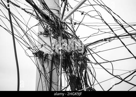 Wirbel von Drähten und Kabeln an einem Mast gegen den klaren Himmel. Salvador, Bahia, Brasilien. Stockfoto