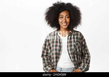 Bild einer schwarzen Frau mit lockigem Haar, lächelnd und glücklich aussehend, in legerer Kleidung auf weißem Hintergrund stehend Stockfoto