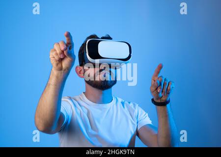 Porträt eines jungen kaukasischen Mannes mit VR-Brille und Interaktion mit der virtuellen Realität. Technologiekonzept der Zukunft. Stockfoto