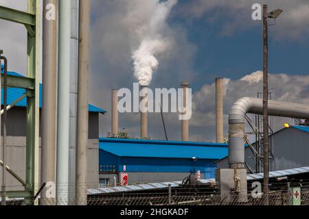 Industriestandort mit dickem weißen Rauch, der von einem der Betonrauchstapel aufsteigt. Konzept für die globale Erwärmung durch die Verbrennung fossiler Brennstoffe. Stockfoto