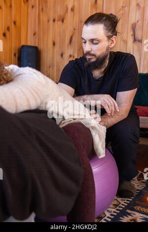 Porträt eines kaukasischen männlichen Shiatsu-Praktizierenden, der die Lebensenergie einer weiblichen Klientin manipuliert, die links vom Rahmen mit dem Kopierraum verschwommen zu sehen ist. Stockfoto