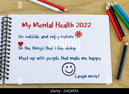 Ziele für psychische Gesundheit 2022 Überschrift mit einer Liste von Ideen, die in einem Notizbuch auf dem Schreibtisch handgeschrieben sind. Konzept der Wohlfühlziele für das neue Jahr. Stockfoto