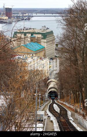 Stadtbild von Kiew mit Blick auf die Kiewer Standseilbahn, den Fluss Dnipro und die Gebäude des alten Podil in der Wintersaison. Vertikales Bild. Stockfoto