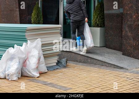 Der Arbeiter lädt Baustoffe und bringt sie für zukünftige Reparaturen in den Eingang. Speicherplatz kopieren. Stockfoto