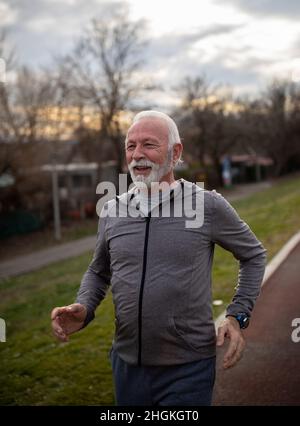 Älterer bärtiger Mann in Sportkleidung, der im Winter draußen auf der Joggingstrecke läuft Stockfoto