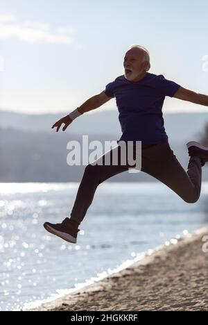 Älterer Mann mit Bart in Sportkleidung, der am Strand springt Stockfoto