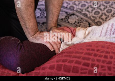 Nahaufnahme der Hände eines männlichen Massagetherapeuten, der Druck auf den äußeren Oberschenkel eines weiblichen Klienten ausübt. Platz nach rechts kopieren. Stockfoto