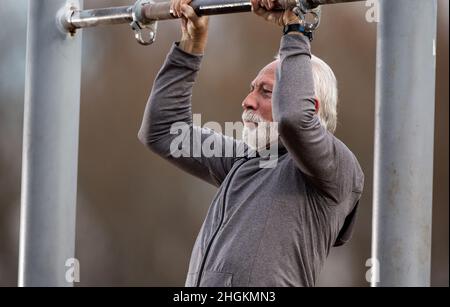 Älterer bärtiger Mann im Trainingsanzug, der Liegestütze im öffentlichen Fitnessstudio im Freien macht Stockfoto