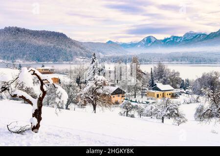Ein Panoramablick auf den verschneiten Faaker See in den österreichischen Alpen. Der See ist von hohen Bergen umgeben. Stockfoto