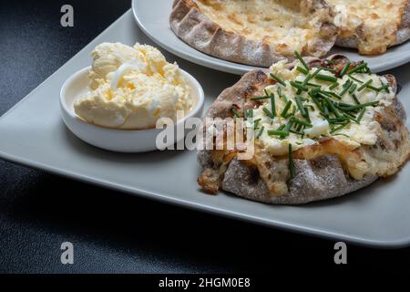 Helsinki / Finnland - 21. JANUAR 2022: Traditionelle finnische Speisen - frische karelische Torten mit Eierbutter und Schnittlauch auf schwarzem Hintergrund. Stockfoto