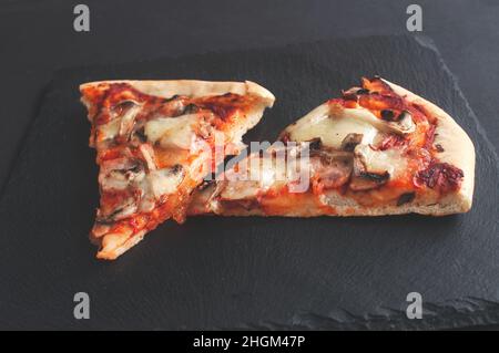 Scheiben frisch gebackene Pizza auf einer schwarzen Tafel auf dunklem Hintergrund Stockfoto