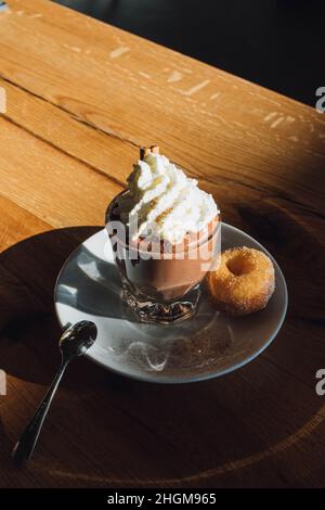 Heiße Trinkschokolade mit Schlagsahne auf dem Teller mit Mini-Donut und Löffel Stockfoto