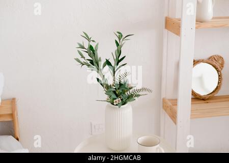 Eukalyptus in einem weißen Topf auf einem weißen Tisch. Helle Innenausstattung mit Holzregal und weißem Tisch Stockfoto