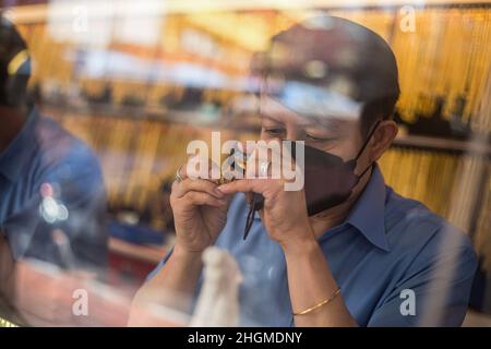 Bangkok, Thailand. 21st Januar 2022. Ein Mitarbeiter, der als Schutzmaßnahme gegen die Verbreitung von Covid-19 eine Gesichtsmaske trägt, überprüft eine Goldkette in einem Goldgeschäft in Bangkoks Chinatown. Goldläden in Bangkoks chinesischer Stadt bereiten sich auf das Geschäft vor dem bevorstehenden chinesischen Neujahr 2022 in Thailand vor. Kredit: SOPA Images Limited/Alamy Live Nachrichten Stockfoto