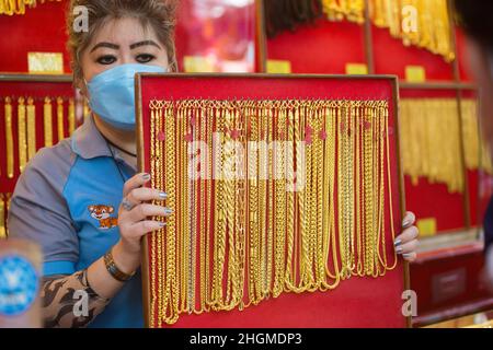 Bangkok, Thailand. 21st Januar 2022. Ein Mitarbeiter, der als Schutzmaßnahme gegen die Verbreitung von Covid-19 eine Gesichtsmaske trägt, hält eine Ausstellung von Goldketten für den Verkauf in einem Goldladen in Bangkoks Chinatown bereit. Goldläden in Bangkoks chinesischer Stadt bereiten sich auf das Geschäft vor dem bevorstehenden chinesischen Neujahr 2022 in Thailand vor. Kredit: SOPA Images Limited/Alamy Live Nachrichten Stockfoto