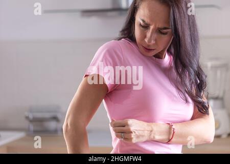Übermäßiges Schwitzen, sichtbar durch Flecken auf einem rosa Hemd einer jungen Frau. Stockfoto