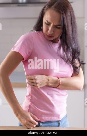 Die Frau sieht sich Schweißflecken an, die auf ihrem rosa Hemd zu sehen sind. Stockfoto