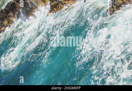 Die Welle trifft am Strand auf den Felsen, das Meerwasser spritzt auf das Meer. Seascape. Spritzer von den Wellen, die gegen das felsige Ufer stoßen. Stockfoto