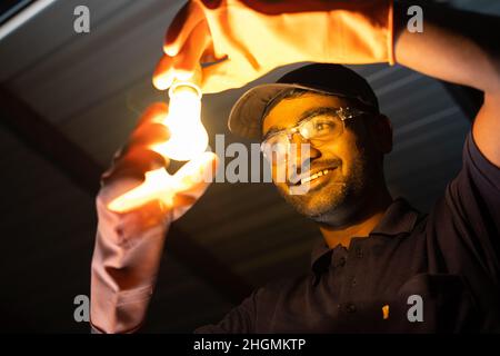 Glücklicher Elektriker nach der Befestigung der Deckenleuchte mit Sicherheitswerkstoffen - Konzept der Reparatur- und Wartungsservice zu Hause mit Sicherheitsvorkehrungen bei Stockfoto