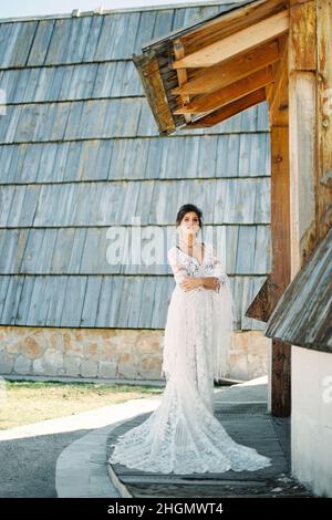 Die Braut im Korbkleid steht an der Schwelle eines Holzhauses Stockfoto
