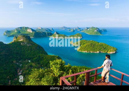 Auf der Terrasse steht ein junger asiatischer Mann in legerer Kleidung, während er im sonnigen Sommer den Blick auf die Inseln entspannt. Mu Koh Ang Thong Nationalpark, Thailand. Stockfoto