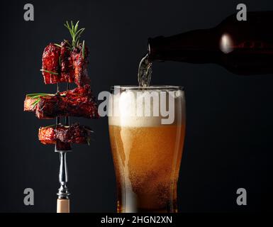 Bier und gegrillter Schweinebauch mit Rosmarin auf einer Gabel. Stockfoto