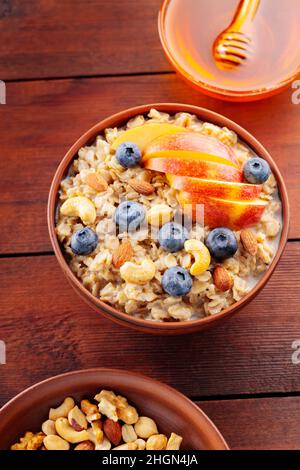 Leckere Haferflocken mit Beeren, Nüssen und Äpfeln auf einem Holztisch. Schüssel Haferbrei mit Heidelbeeren und Honig. Gesundes Frühstück. Draufsicht Stockfoto