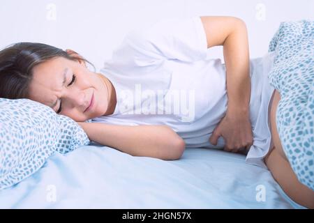 Frau im Bett, die an Menstruationsschmerzen, Bauchschmerzen oder Bauchschmerzen leidet. Menstruationszeit oder PMS Stockfoto