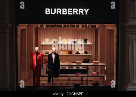 Beschilderung zum Burberry-Geschäft und Schaufenster. Eine britische Luxusmarke für Bekleidung und Mode-Accessoires. Zwei weibliche Schaufensterpuppe in eleganter schicker roter Jacke gekleidet Stockfoto