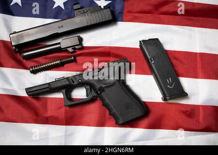 Nahaufnahme einer zerlegten Pistole auf der amerikanischen Flagge. Waffengesetze in den USA. Handfeuerungsteile. Draufsicht Zerlegung Waffe, Waffenpflege. Glock 19. Stockfoto