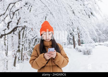 Einsame asiatische Frau im Winterpark, traurig und deprimiert, müde und gefroren, in warmen Kleidern gekleidet Stockfoto