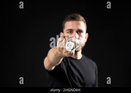 Der Mensch hält eine ethereum-Münze. Junger bärtiger Mann mit virtueller Währung ethereum. Stockfoto