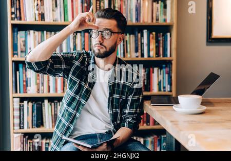 Nachdenklicher junger Mann, der in der Bibliothek lernt und studiert Stockfoto