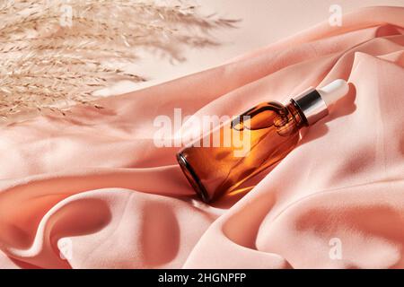 Ätherisches Öl zur Hautpflege in einer braunen Glasflasche mit einer Pipette auf einem Seidentuch. Kosmetisches medizinisches Schönheitsprodukt für Aromatherapie Stockfoto