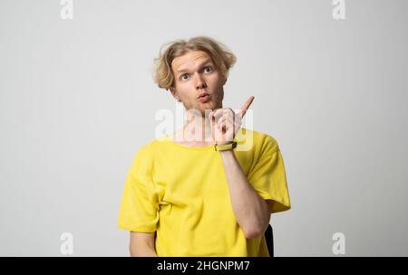 Der junge Hipster-Mann trägt ein gelbes T-Shirt, das mit Hand und Finger zur Seite zeigt, da er eine gute Idee hat. Stockfoto