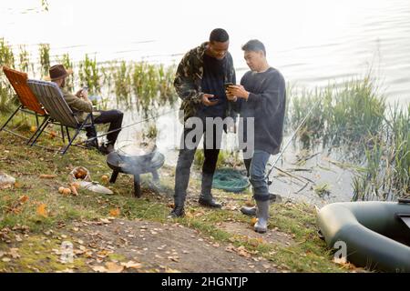 Männer mit Smartphones während der Ruhe an der Teichküste Stockfoto